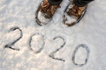Brown leather shoes standing on the snow with inscription 2020. New Year holiday background.