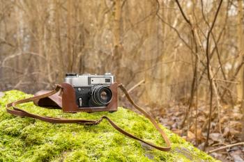 Retro camera on the mossy stone with forest background. Traveling with photo camera, photography as hobby concept