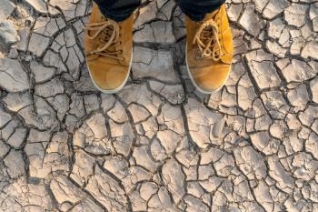 Human feet standing on dried earth. Drought and salinization. Soil salinity. Cracked ground. Ecological disaster