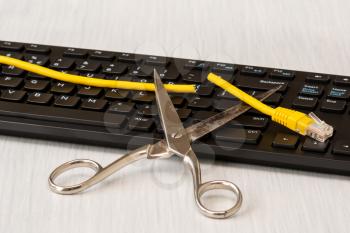 Scissors and cutted network cable over computer keyboard. Radical disconnection internet
