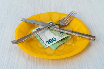 Money lying on the plate with fork and knife. Food expenses concept.