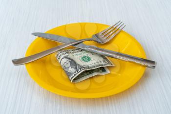 US dollar lying on the plate with fork and knife. Food expenses concept.