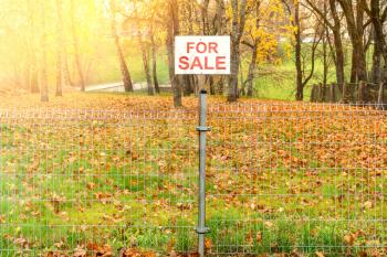 Real estate conceptual image. Land for sale sign  behind the metal fence.