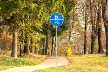Blue sign of a bike path and a pedestrian in the park during autumn season