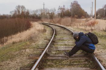 Man sitting alone on the railroad and close the face with a hands, felling sad worry regret or fear. Unreccognizible person with covered face.