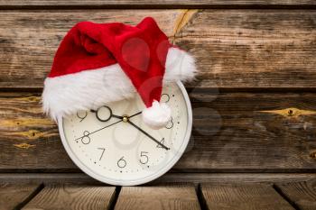 Christmas time - wall clock with Santa hat on wooden background