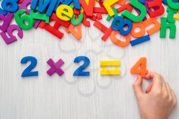 Child playing with magnetic numbers and letters. Simple mathematic formula 2 x 2 = 4.