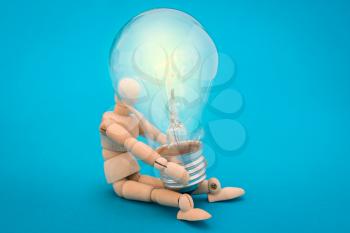 Wooden doll holds a glowing light bulb, on blue background. Concept ideas.