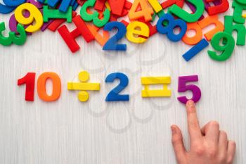 Child playing with magnetic numbers and letters. Simple math formula 10 : 2 = 5
