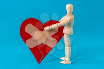 Bad relationships, breaking up, sadness emotions concept. Wooden man holding broken heart fixed with plaster bandage.