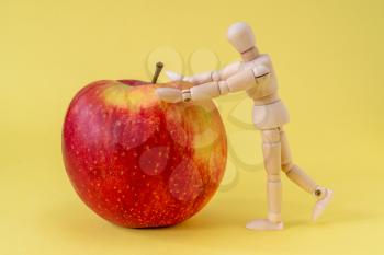 Wooden man pushes a healthy red apple on the yellow background