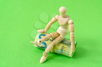 Wooden man sits on the roll of Euros. Investment or savings concept.