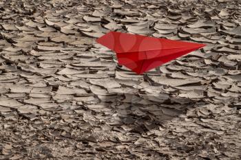 Red paper plane flying over dry soil. Concept for climate change, global warming.