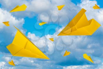 Yellow paper planes flying in a cloudy sky. Travel concept.