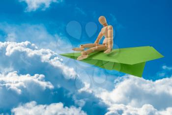 Wooden man sitting on the paper plane and flying over clouds. Follow your dreams, life goals, and taking flight concept. 