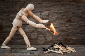 Wooden man ignites the bonfire with matches on the wooden background. Unsafe behaviour, dangerous situation at home.