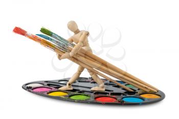 Wooden man standing on the watercolor palette and holding paintbrushes. Copy space.
