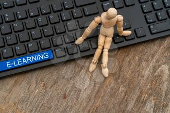 Wooden man sitting on the keyboard with E-learning button, internet concept