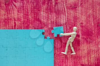 Wooden mannequin with blue puzzle on pink background. Building a business success.