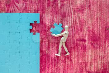 Wooden mannequin with puzzle on pink background. Building a business success.