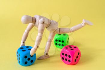 Wooden man figure with game dice on yellow background.