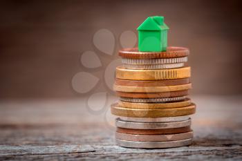 Green miniature home on the stack of various coins. Home loan refinance. Real estate sales.