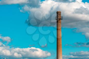 An old factory brick chimney against a cloudy blue sky.