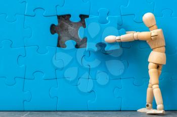 Wooden man assembling last missing puzzle on puzzle wall. Creating or building own business concept.