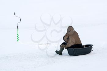 Winter fishing on lake. Fisherman and ice drill  on frozen lake. Rear view.