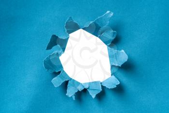 Breakthrough paper hole. Torn ripped blue paper sheet with round hole in the center and white background