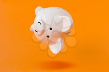Piggy bank falling on the orange background. Financial concept.