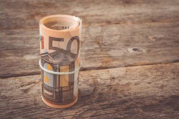 Roll of fifty euro banknotes on the old wooden background