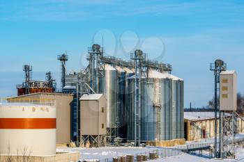 Snowy silos in winter. Industrial elevator dryers, building exterior, storage and drying of cereals, wheat, corn, soybeans, sunflowers. 