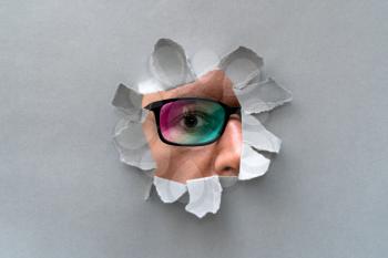 Man in glasses peeping through hole on paper. Male in color glasses looking through hole. 