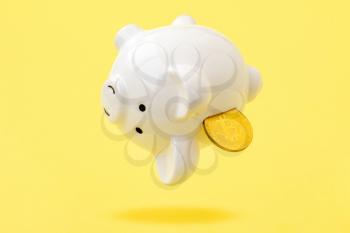 Piggy bank with bitcoin coin falling down on the yellow background. Risks and dangers of investing to bitcoin.