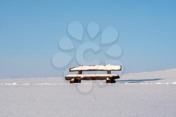 Empty bench in snowy field under a blue sky. Winter landscape.