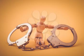 Wooden man with handcuffs on hands sitting on yellow background. Conceptual image.