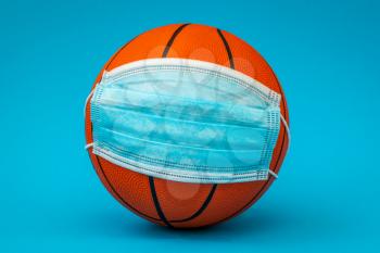 Basketball ball with surgical medical face mask on the blue background. Concept for Coronavirus COVID 19 pandemic and epidemic affecting basketball seasons game suspend.