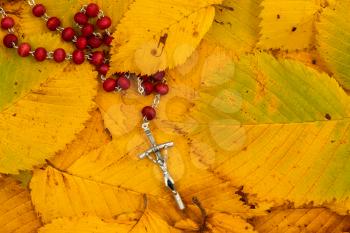 Silver crucifix under fallen leaves, religion concept