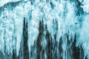 A frozen waterfall with ice in a blue and white color in winter. Winter background.
