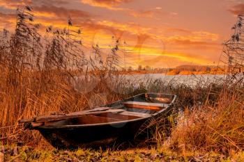 An old wooden boat left near the lake, used by local people for fishing, boat in poor condition.Beautiful sunset sky on background.