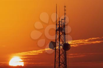 Silhouette of communication tower against sunset background.
