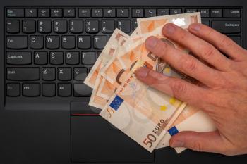 Conceptual shot of businessman's hand taking euro banknotes from computer keyboard. Financial help or government aid, for people affected by the crisis