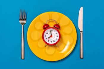 Alarm clock on yellow plate with fork and knife. Intermittent fasting, Ketogenic dieting, weight loss, meal plan and healthy food concept