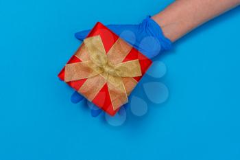 Hand in protective glove gives gift box. Pandemic winter holidays celebration. Quarantine hygiene. 
