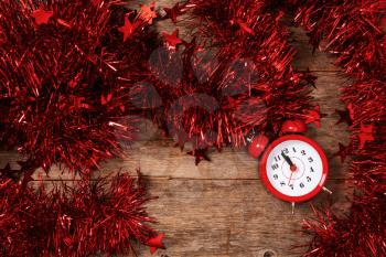 Counting last moments before Christmas or New Year. Countdown to midnight. Red alarm clock lying on table in bright garland and tinsel close up.