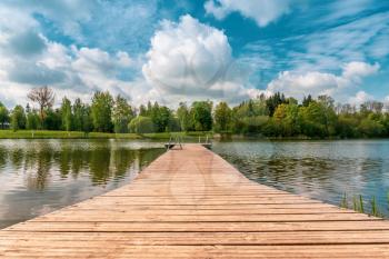 Mole (pier) on the lake. Wooden bridge in forest in spring time with calm lake. Lake for fishing and recreation with pier. 