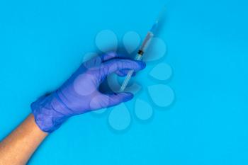 Hand in blue glove holding syringe with copy space. Syringe with sharp needle in hand. Medical treatment concept. Vaccination concept.