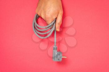 Hand holds electric cable with plug on a pink background. Copy space.