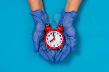 Hands in medical gloves holding red alarm clock. The concept of time to the end of the pandemic corona virus